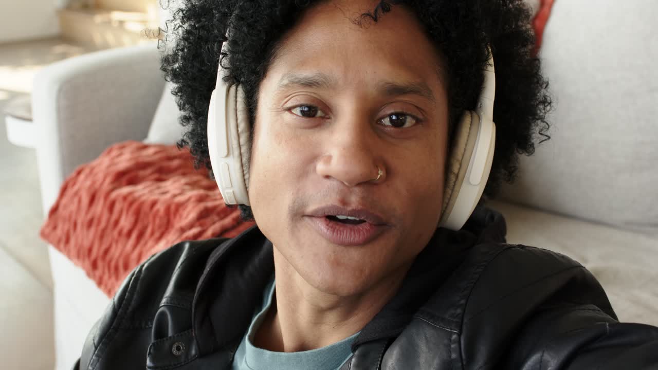 Uomo afroamericano di mezza età con le cuffie apre la bocca e conduce un podcast su un divano grigio.