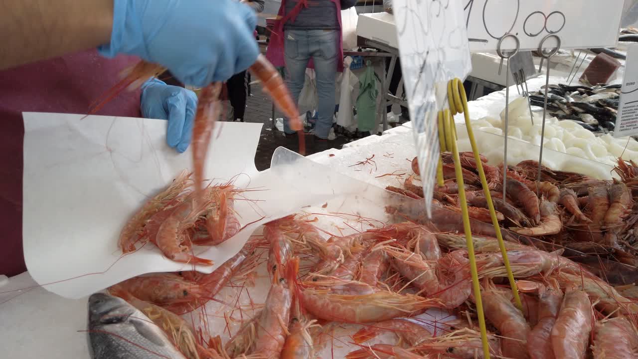 el vendedor toma gambas rojas y las pone en la hoja de papel, vendiendo pescado en el mercado