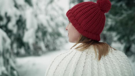 caucasian woman wearing red hat walking in snowing forest.