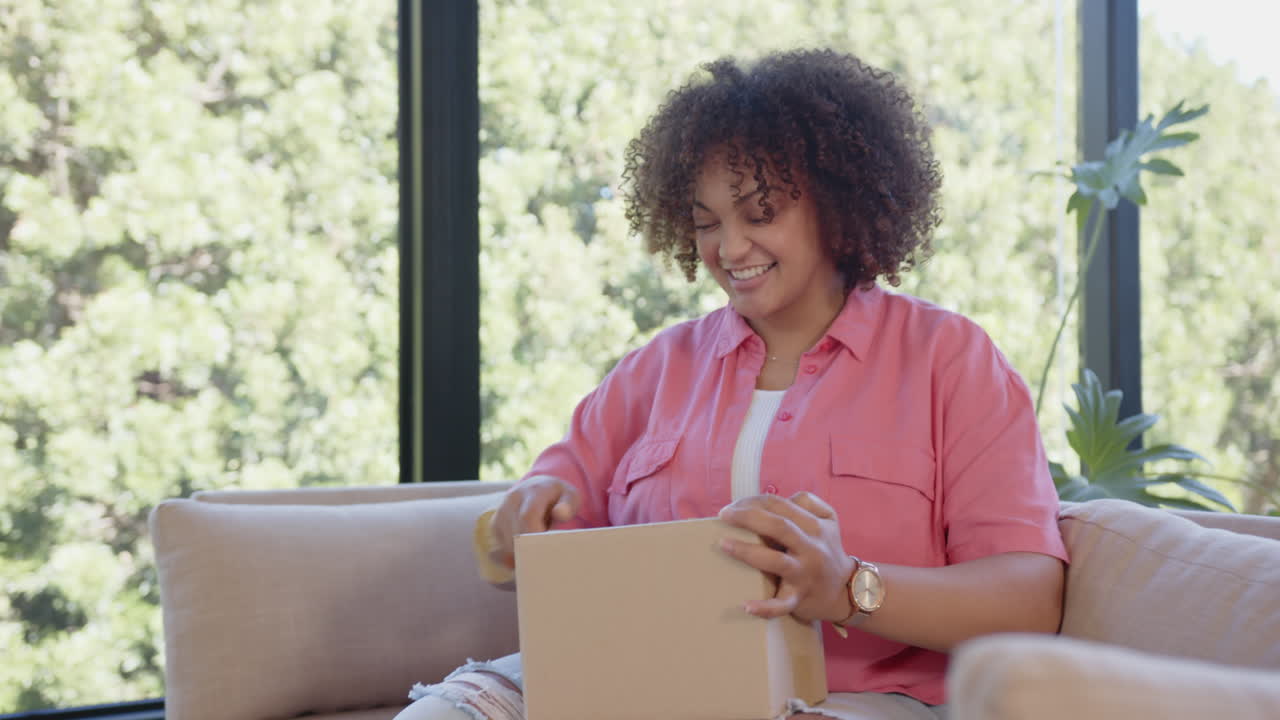 Opening cardboard box, excited woman sitting on couch in living room