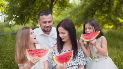 family enjoying watermelon at a picnic in the park