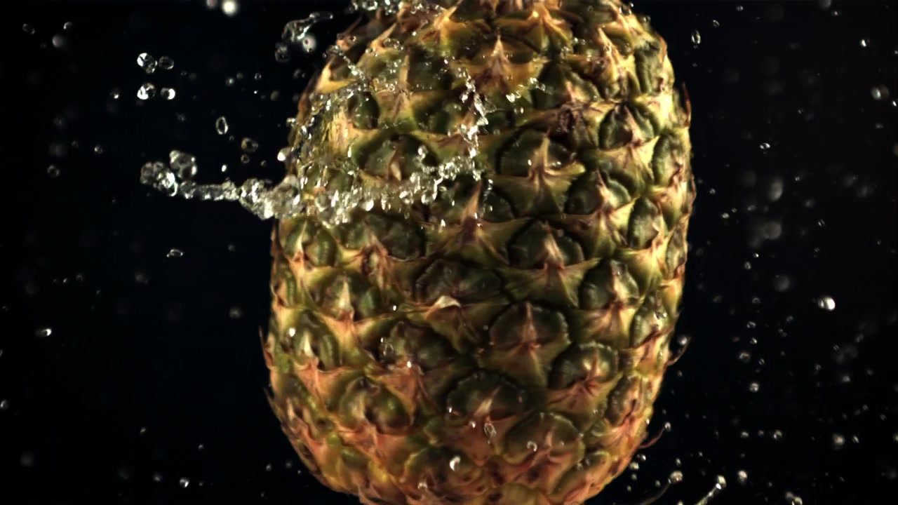 Frische Ananas mit Wasserspritzern auf schwarzem Hintergrund in Zeitlupe