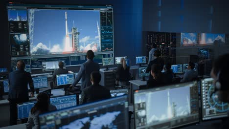 group of people in mission control center witness successful space rocket launch. flight control employees sit in front computer displays and monitor the crewed mission. team stand up and clap hands.