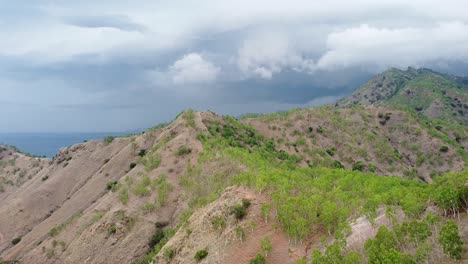 Rising-over-vast-rocky-mountain-ranges-with-sparse-greenery,-trees-and-plants-during-the-dry-season-on-remote-tropical-island