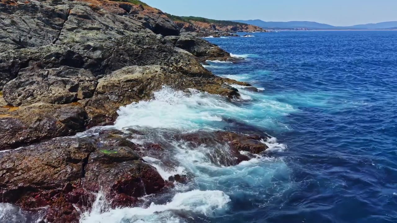 Onde che si infrangono contro la costa rocciosa sotto un cielo sereno in una zona costiera d'estate