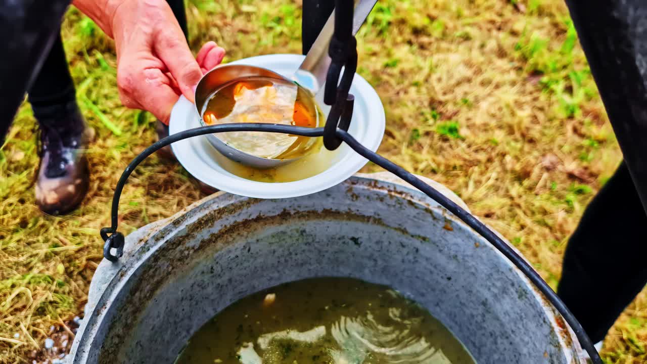 Soup stirred with ladle as vegetable chunks swirl around and poured into paper bowl