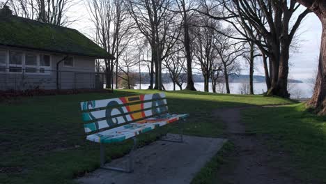 Colorful-park-bench-in-a-public-park-by-the-sea-with-people-walking-by-in-the-background