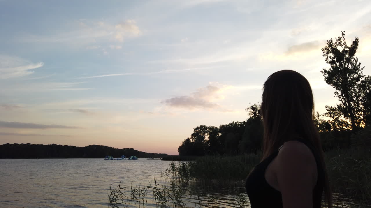 小さな桟橋にいる女性の映画のショットは、日没時の素晴らしい湖を賞賛します-1