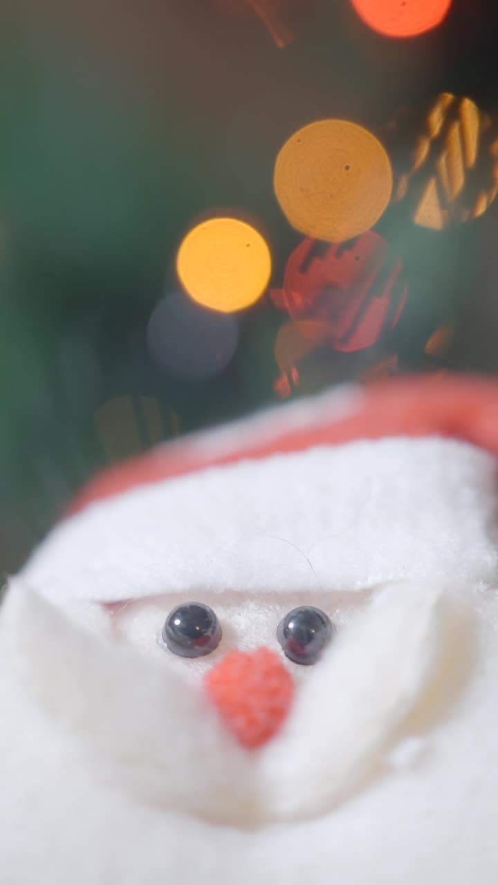 A close-up of a Santa Claus figurine with blurred Christmas lights in the background