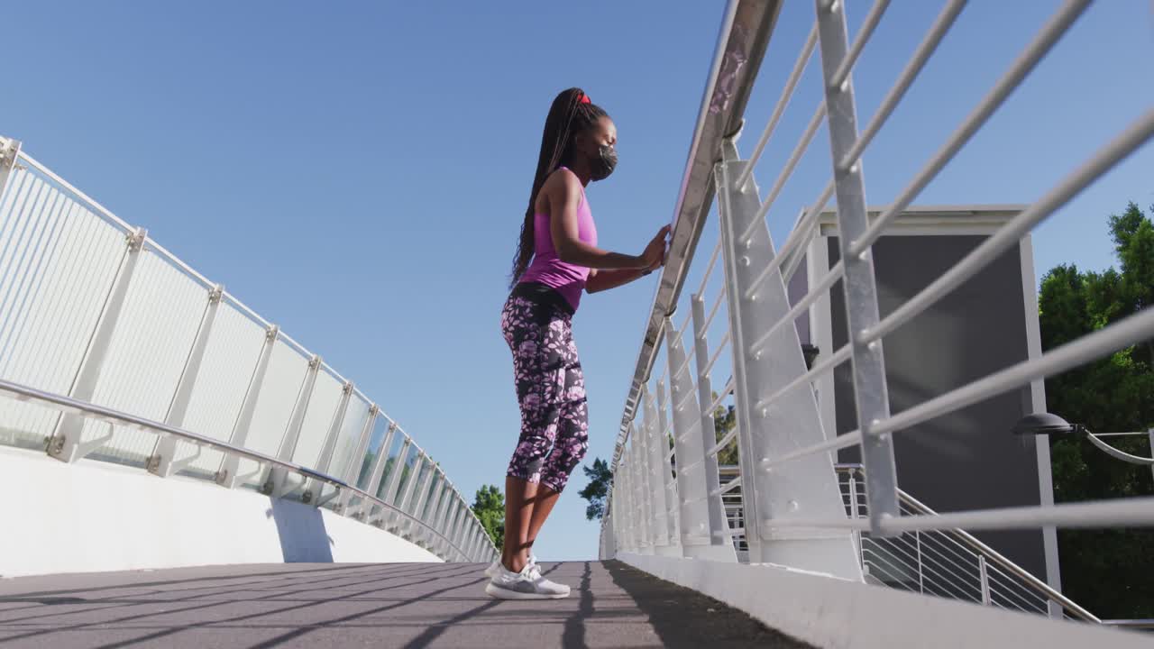 mujer afroamericana estirando su pierna sosteniendo la barandilla del puente de la ciudad
