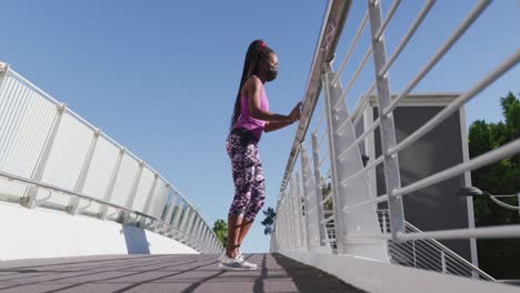 African-american-woman-stretching-her-leg-holding-the-railing-of-the-city-bridge