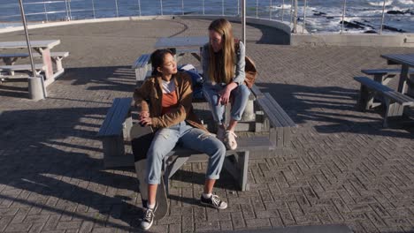 high angle view of a caucasian and a mixed race girl talking sitting on a table