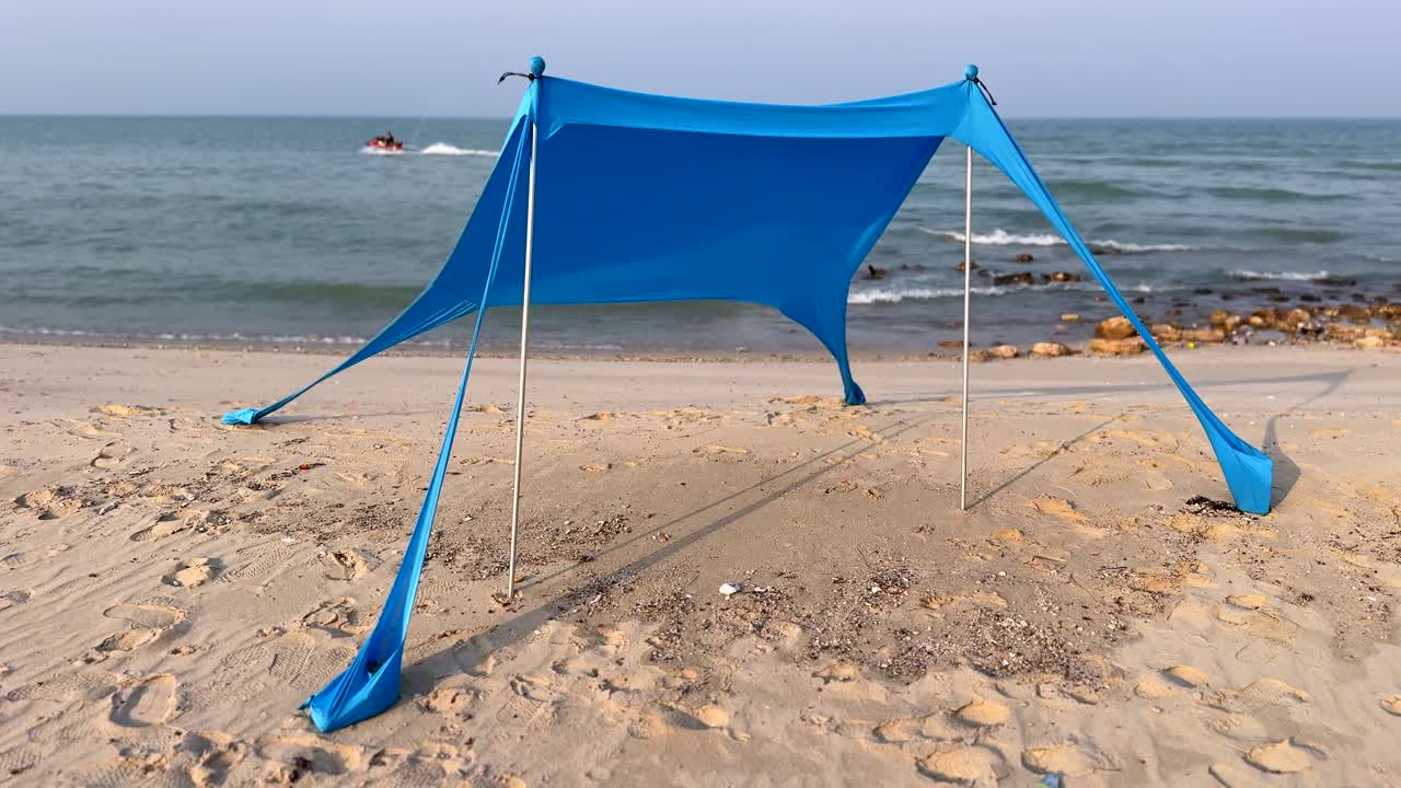 A vibrant blue beach tent stands on the sandy shore, perfect for beach vacations, outdoor activities, and coastal relaxation scenes