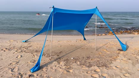 a vibrant blue beach tent stands on the sandy shore, perfect for beach vacations, outdoor activities, and coastal relaxation scenes