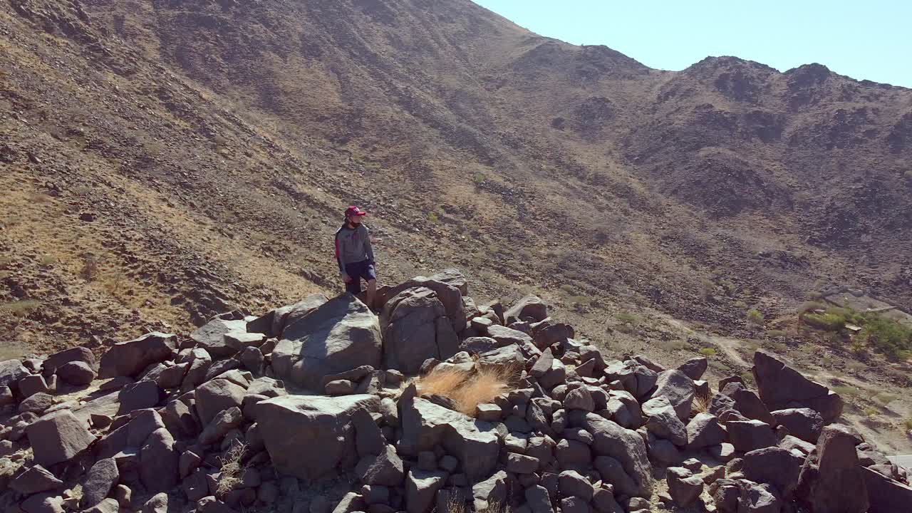 A guy hiking or climbing on a rocky mountain top with drone shot