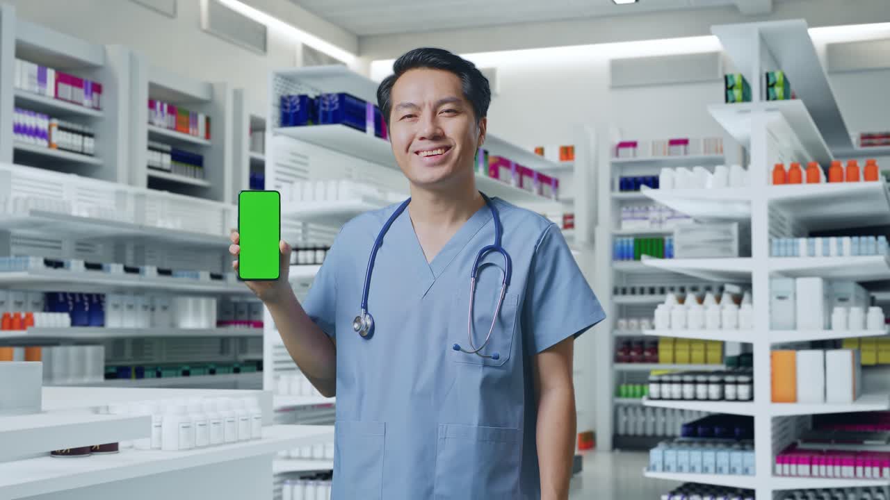 스테토스코프를 들고 있는 아시아 남성 의사 가 약국 에 서 있을 때 초록색 스크린 의 스마트폰 을 보여주고 미소 짓고 있다