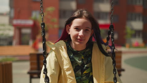 girl with dark straight hair sits on swing in modern city