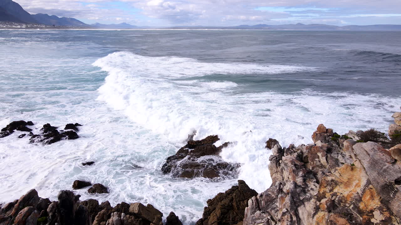 Aerial slow motion view of waves crashing onto jagged Hermanus coastline