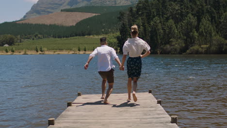 happy couple running jumping off jetty in lake splashing in water having fun summer vacation