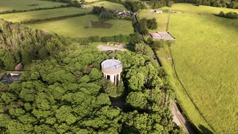 Aerial-View-Of-Water-Tower-Amidst-Dense-Trees-In-A-Countryside-Near-Essex,-United-Kingdom