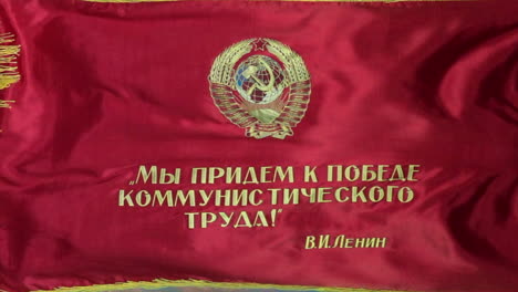 Zoom-out-on-Soviet-parade-flag-with-hammer-and-sickle-emblem-flying-in-slow-motion-with-vivid-blue-sky-in-background