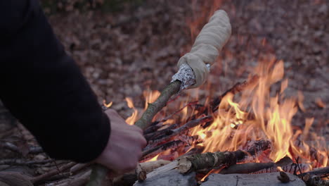 una mujer asando un pan en un palo sobre un fuego de campamento