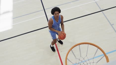 high angle of african american male basketball player shooting ball at hoop on court, slow motion