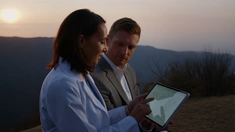 two professionals discussing data on a tablet during sunset