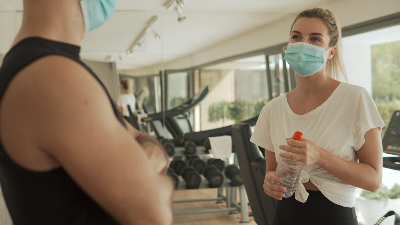 코로나19 팬데 기간 동안 체육관에서 대화를 나누는 얼굴 마스크를 착용한 여성과 남성.