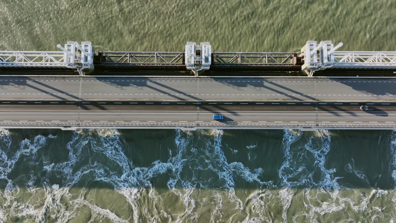 toma aérea de agua que fluye a través de una barrera abierta de marejada ciclónica del este de scheldt, y tráfico que pasa por encima de ella, en un hermoso día soleado en zelanda, los países bajos