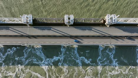 aerial overhead shot of water flowing through an open eastern scheldt storm surge barrier, and traffic driving over it, on a beautiful sunny day in zeeland, the netherlands