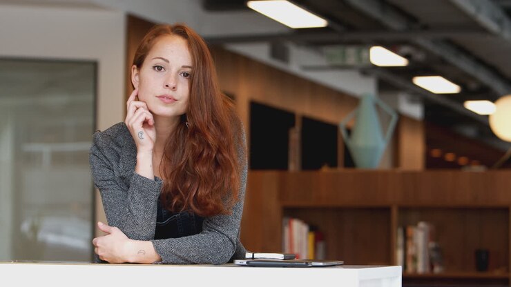 Ritratto di giovane imprenditrice casualmente vestita in piedi nel moderno posto di lavoro a pianta aperta