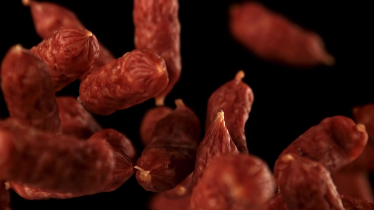Salsicce di salame che cadono al rallentatore su sfondo nero