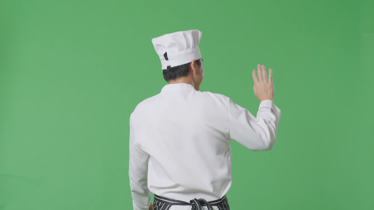 vista trasera del chef asiático caminando y agitando la mano en el estudio de fondo de la pantalla verde