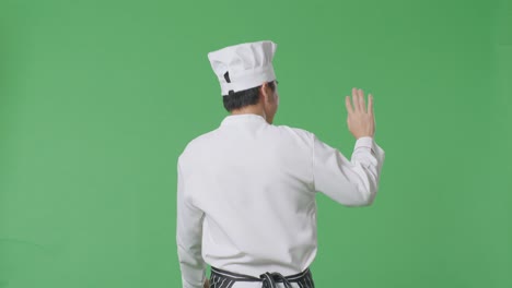 vista trasera del chef asiático caminando y agitando la mano en el estudio de fondo de la pantalla verde