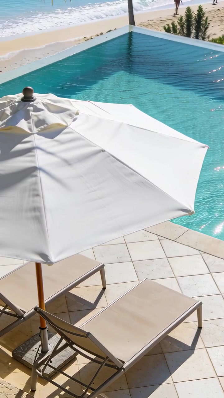 Vertical video: Panning camera revealing white parasol and beige chairs poolside with shore walkers
