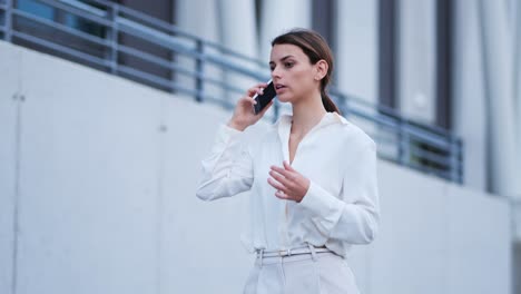 una mujer de negocios camina a lo largo de una pared mientras habla en su teléfono celular