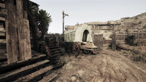 a covered wagon stands outside of a wooden building in a dusty, western town.