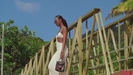 ángulo bajo de una chica negra caminando por un puente en un traje de playa en una playa tropical
