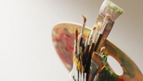 Video-of-a-collection-of-paintbrushes-in-a-jar-and-used-palette-on-pale-background-with-copy-space