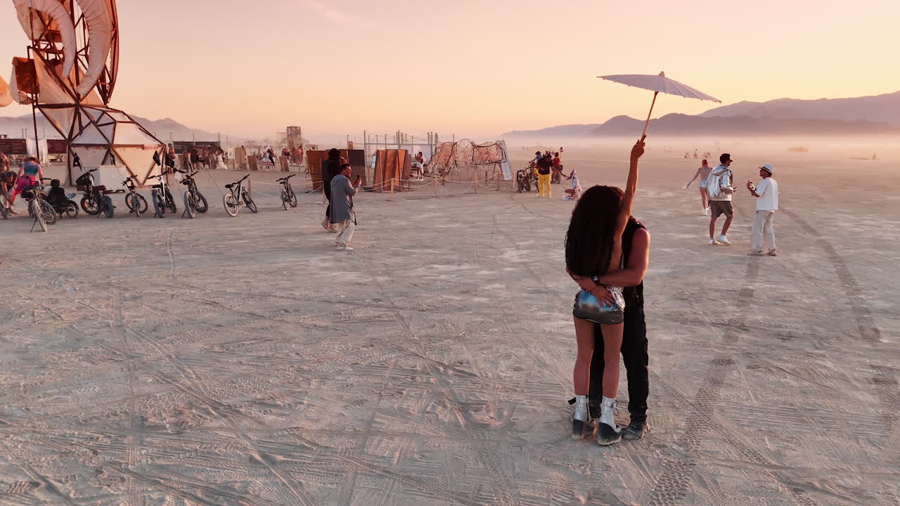 Nevada, USA, 25 August 2025: A couple shares a romantic moment under the pink sunset sky at Burning Man surrounded by art and other participants