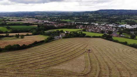 Vuelo-Aéreo-Sobre-Tierras-De-Cultivo-En-East-Devon-Con-Tractor-Cosechando-Heno