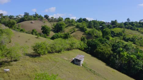 Sobrevuelo-Aéreo-Colinas-Verdes-Con-Casas-Diminutas-Durante-El-Día-Soleado-Y-Cielo-Azul-En-El-Caimito---Campo-De-República-Dominicana