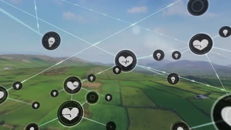 Animation-of-connected-icons-over-aerial-view-of-green-field-against-mountains-and-cloudy-sky