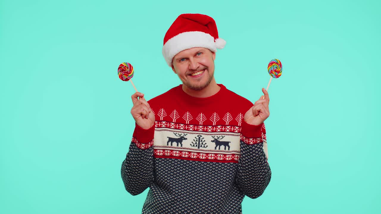 빨간 새해 스웨터를 입은 재미있는 남자는 사탕 줄무늬 막대사탕을 들고 그 뒤에 숨어서 장난을 치고 있습니다