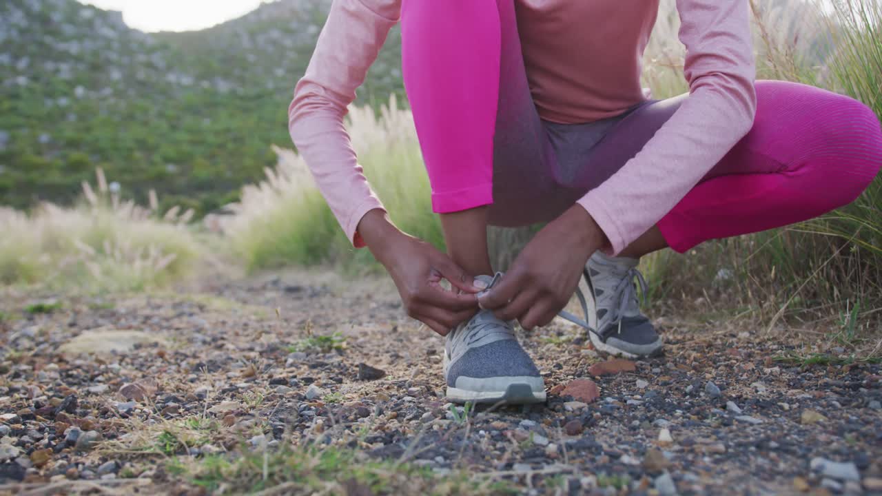 Donna di etnia mista che si allaccia la scarpa mentre si allena in campagna.