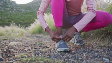 Low-section-of-mixed-race-woman-exercising-tying-her-shoe-in-countryside