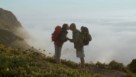 pareja mayor parada en la montaña, tomándose de la mano y besándose