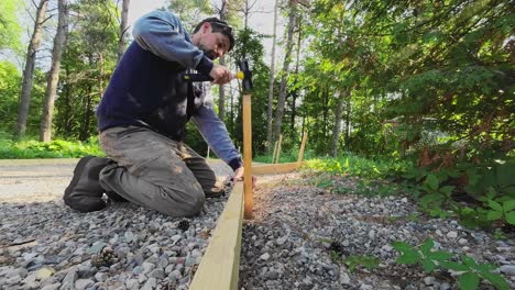 closeup shot of a carpenter hitting wooden staked into the ground, outdoor formwork construction project.