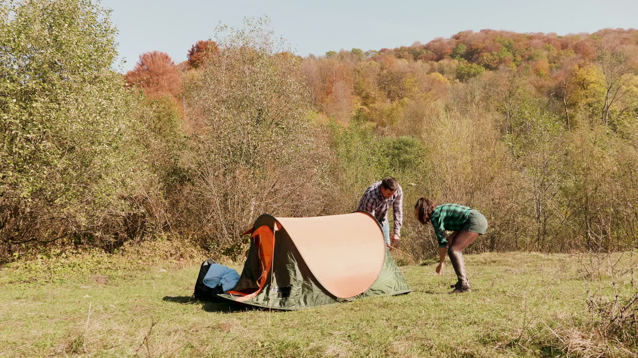 una hermosa pareja de jóvenes ayudándose mutuamente a montar la tienda de campamento